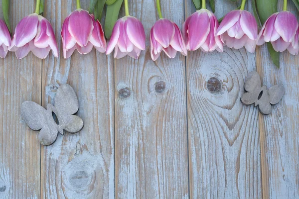 Old grey blue wooden background with pink white tulips border in a row  and empty copy space with wooden spring summer butterflies decoration