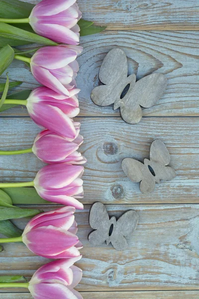 Old grey blue wooden background with pink white tulips border in a row  and empty copy space with wooden spring summer butterflies decoration