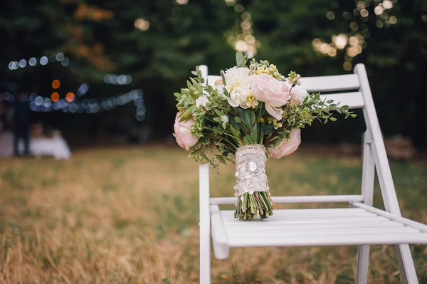 Wedding bouquet of peonies flowers and greenery standing on vintage stool and bokeh lights on background