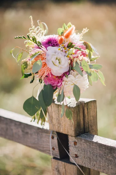 Wedding bouquet of white and violet flowers and greenery standing on wooden fence