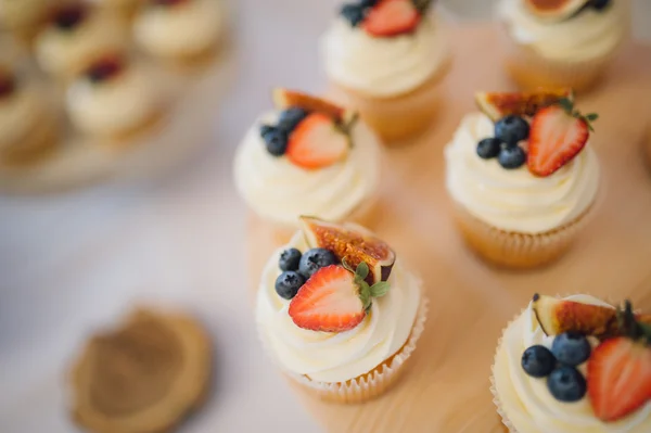 White cupcakes with cream decorated with strawberries and blueberries costs on a wooden plate