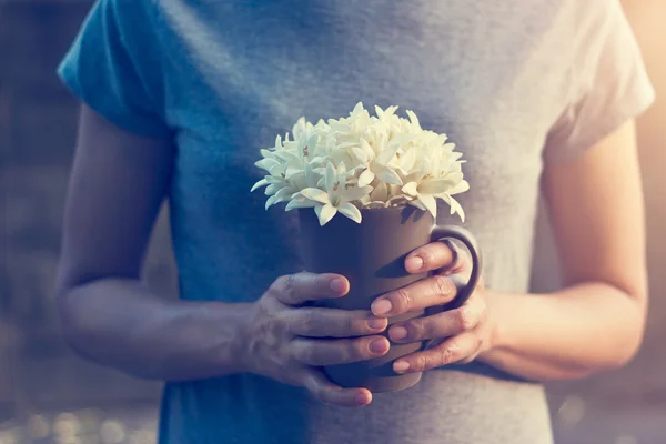 Woman hands holding white flowers in cup on falling flowers background