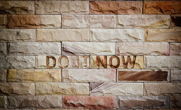Do it now text on brown brick wall