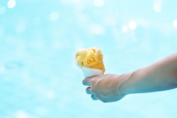 Woman holding melting ice cream in waffles cone in hand over pool