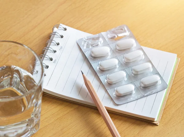 Pills in blister pack with note pad and pencil, Patient take note