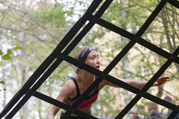 Blonde woman covered with mud climbing a net obstacle