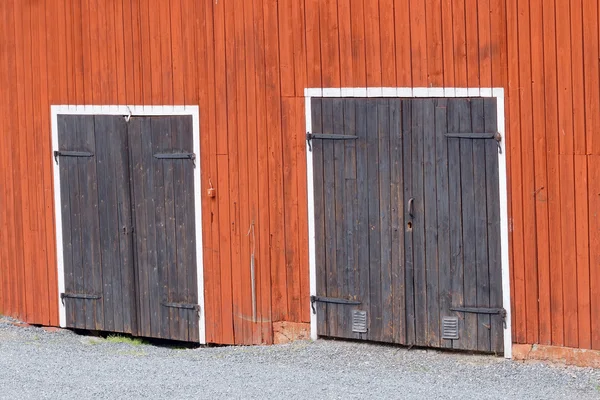 Two black doors in a red barn wall
