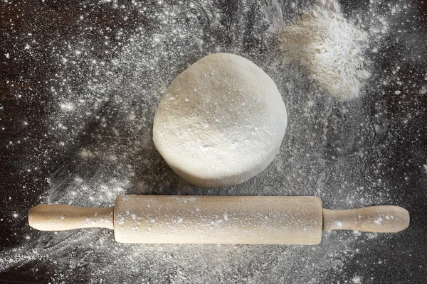 Dough and rolling pin with flour sprinkled lie on the kitchen ta