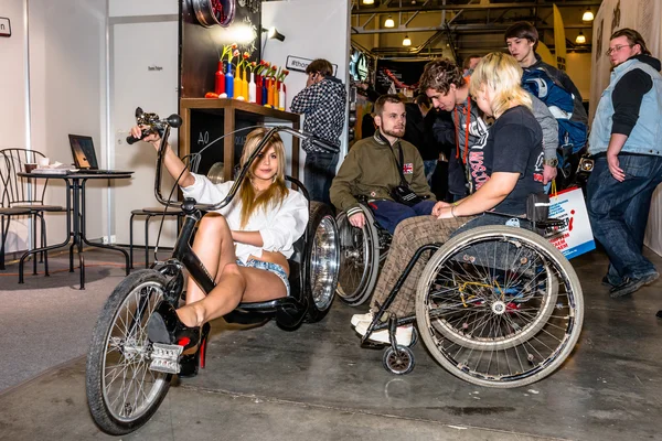 Motopark-2015 (BikePark-2015). Thomi Felgen tuning studio. People in wheelchairs are watching the stand and they are talking with girl on the original bicycle (handmade).