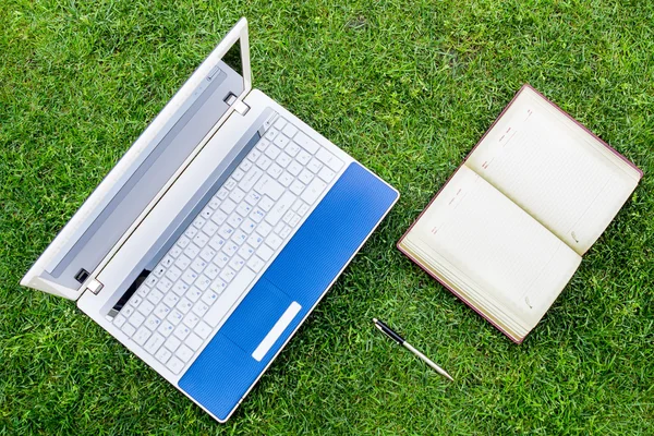 White Laptop, notebook and pen Placed On Green Grass Field. Flat lay.