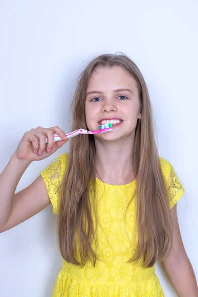 Young girl in a yellow dress brushing her teeth