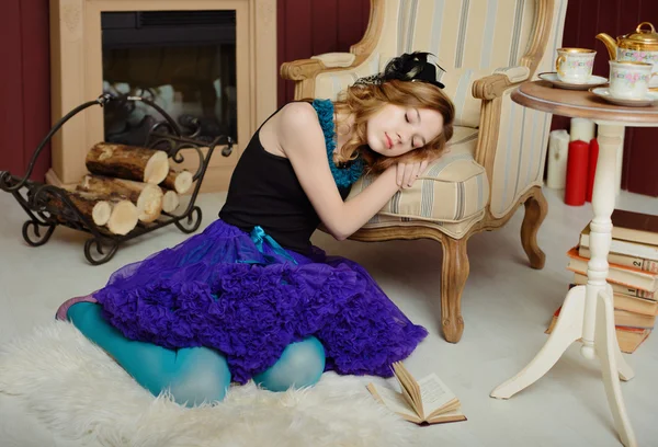 Young girl in the image of Alice in Wonderland fell asleep near the fireplace