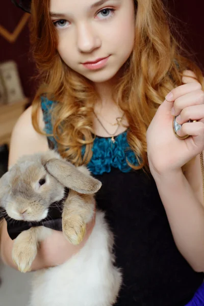 A young girl in the image of Alice in Wonderland holds a rabbit and pocket watches