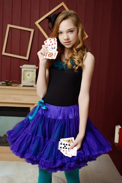 Young girl in the image of Alice in Wonderland stands near the fireplace and holds a playing cards