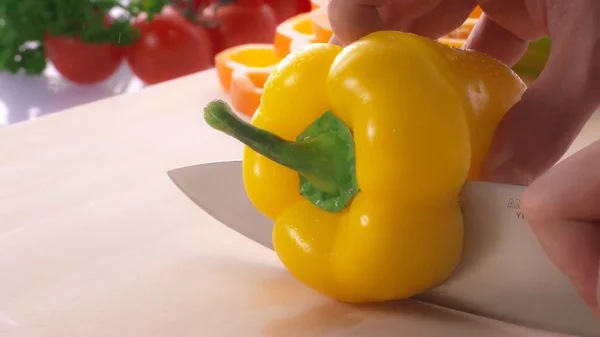 Slicing a yellow pepper with knife on the kitchen table.