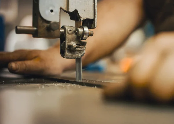 Craftsman cutting an iron rod using a hacksaw.