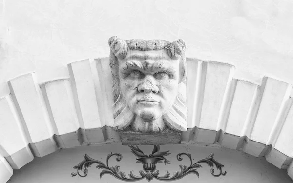 Devil head carved above the stone arch of an Italian villa.