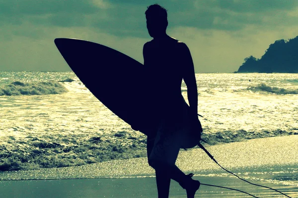 Silhouette of surfer with a board on a sunset evening in Manuel Antonio's National Park main beach, Costa Rica