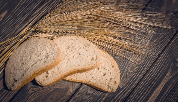 Slices of bread and rye spikelets on the background of natural wood