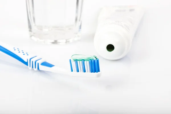 Dental care equipment on white background, stripe toothpaste on toothbrush, glass of water, paste tube,