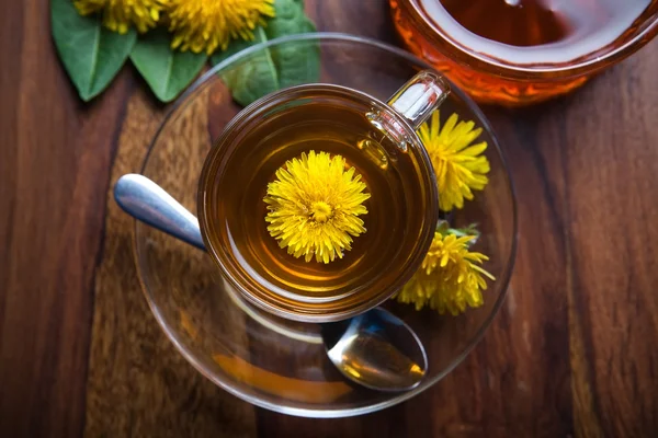 Dandelion herbal tea with fresh yellow blossom in tea cup, on wooden table