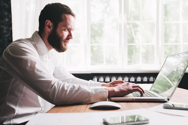 Man working at the office next to a window using a laptop