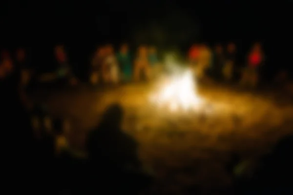People sit at night round a bright bonfire. blurred
