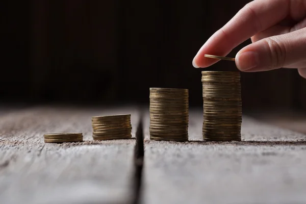 Hand putting coins to a stack on a wooden background