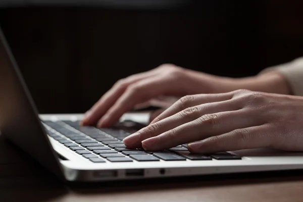 Woman hands using laptop at office desk, with copyspace in dark