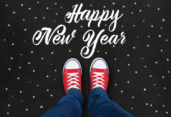 Feet wearing red shoes on black background with Happy New Year t