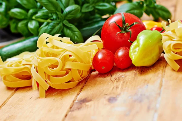 Raw tagliatelle with vegetables on wooden table