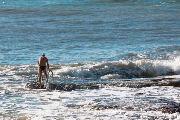 Senior man with swim cap prepares to swim in rough sea