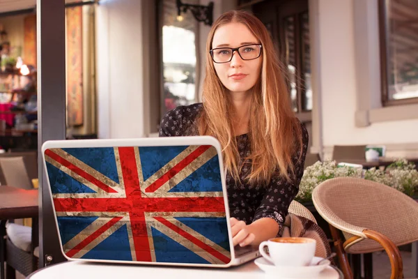 Young  woman sitting in a cafe with notebook with flag of Great Britain