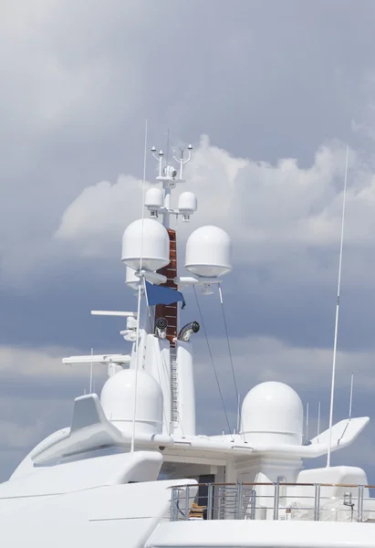 Upper deck of a white super yacht with navigational radars and satellite TV antenna on cloudy rainy summer day