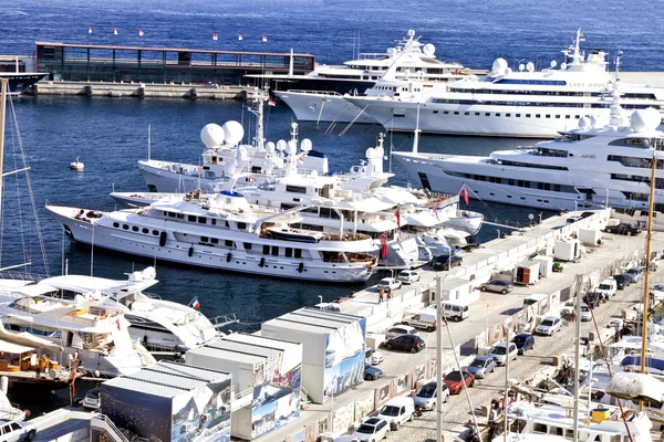 Super yachts, sailing boats and ships docked in Monte Carlo, Monaco harbor , by a pier with parked cars.