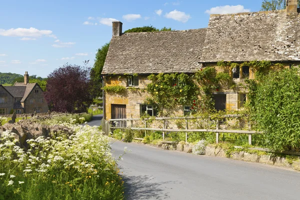 Road through rural hillside  English village with traditional  golden coloured stone cottages, wild flowers