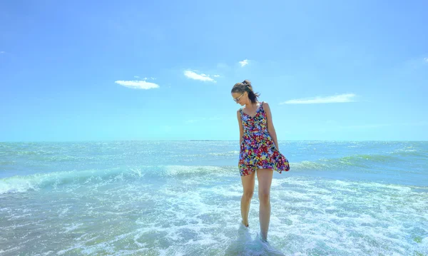 Young smiling woman standing in sea waves and holding her dress
