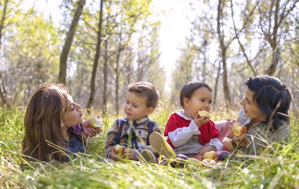 Two mothers with their kids eating apples in the forest