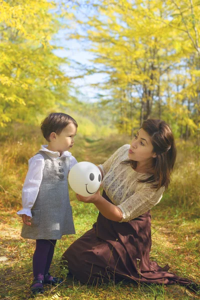 Mother and daughter in forest with balloon in autumn