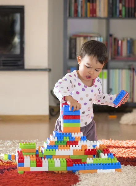 Brunette girl of preschool age playing with colorful blocks sitting on a floor