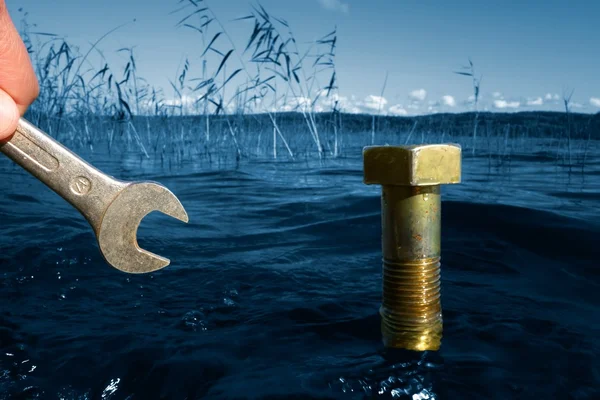 Nature protection concept: Fingers holding tool nearby massive bolt in blue lake water