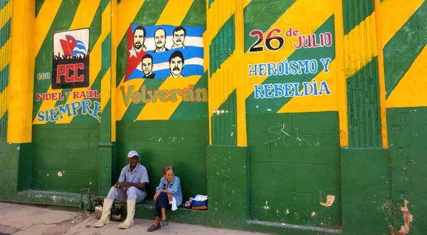 Unidentified Cuban male and female sitting underneath colorful revolution Mural in Havana, Cuba.