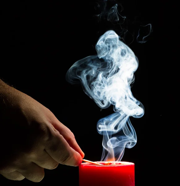 Mans hand is lighting a candle. Smoke