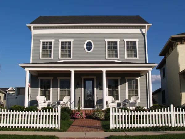 New two story vinyl home built to look like an old historical house with gray vinyl siding and large front porch.