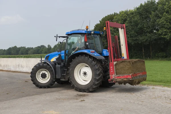 Blue tractor with a red bale slicer