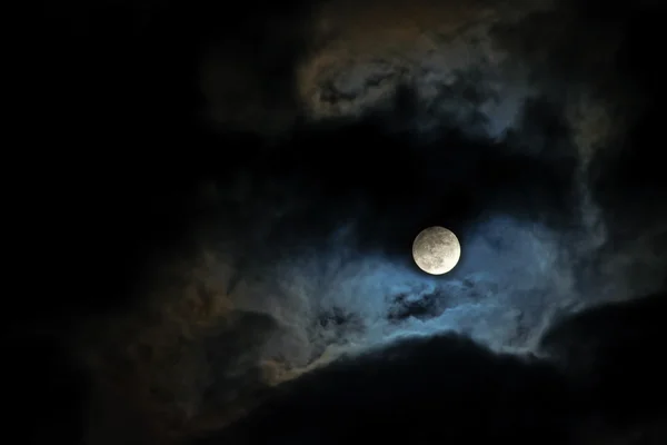 Full moon lights up the clouds on the dark night sky, copy space