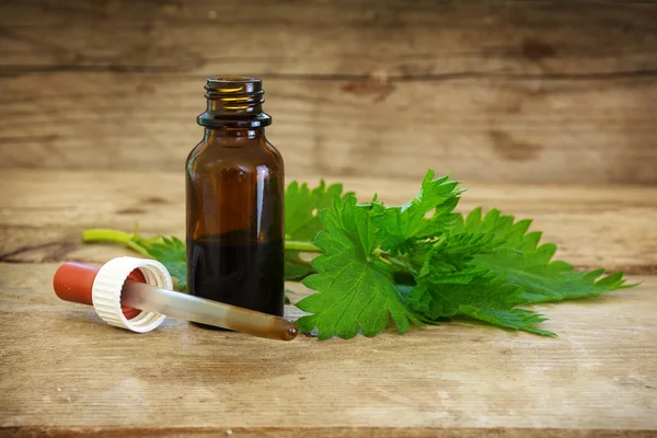 Nettle tincture in a small bottle and fresh leaves on a rustic wooden background