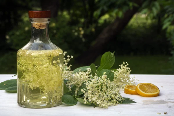 Homemade elderflower syrup  in a glass bottle on a white table in the garden