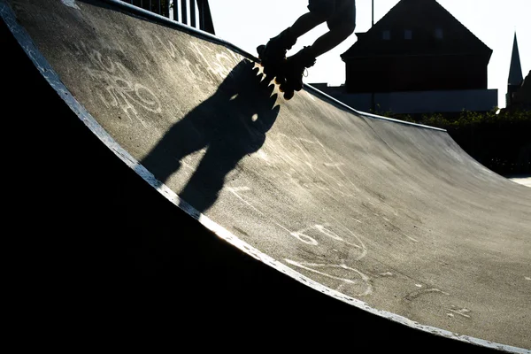 Feet of a rollerblader with inline skates riding over the halfpipe  in an outdoor skate park,  backlit