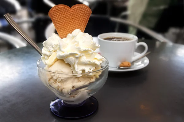 Sundae with ice cream, whipped cream and biscuit and a cup of coffee on a metal table in a shady street cafe